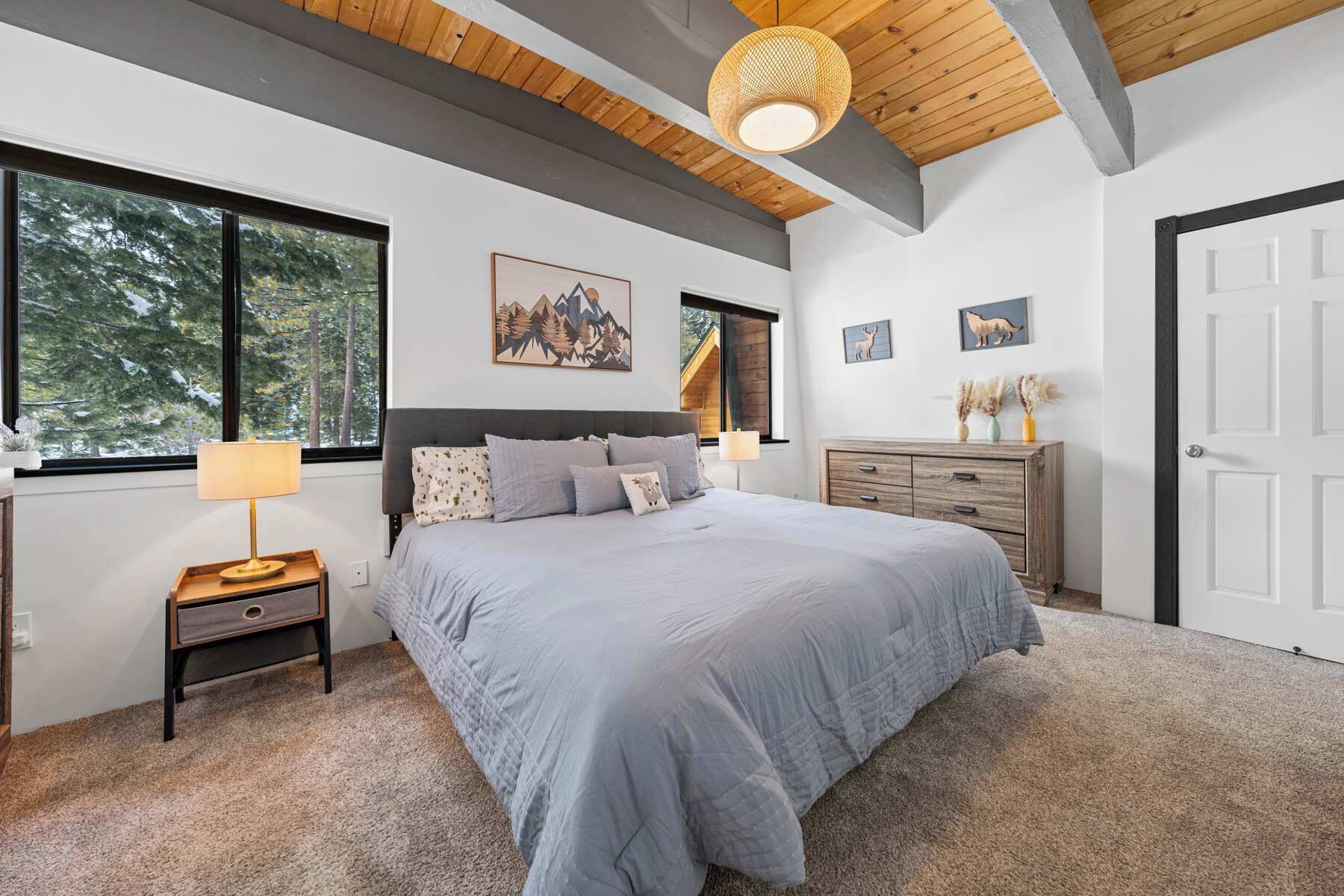 A bedroom with a large bed, a nightstand, a dresser, and a window with a view of trees.