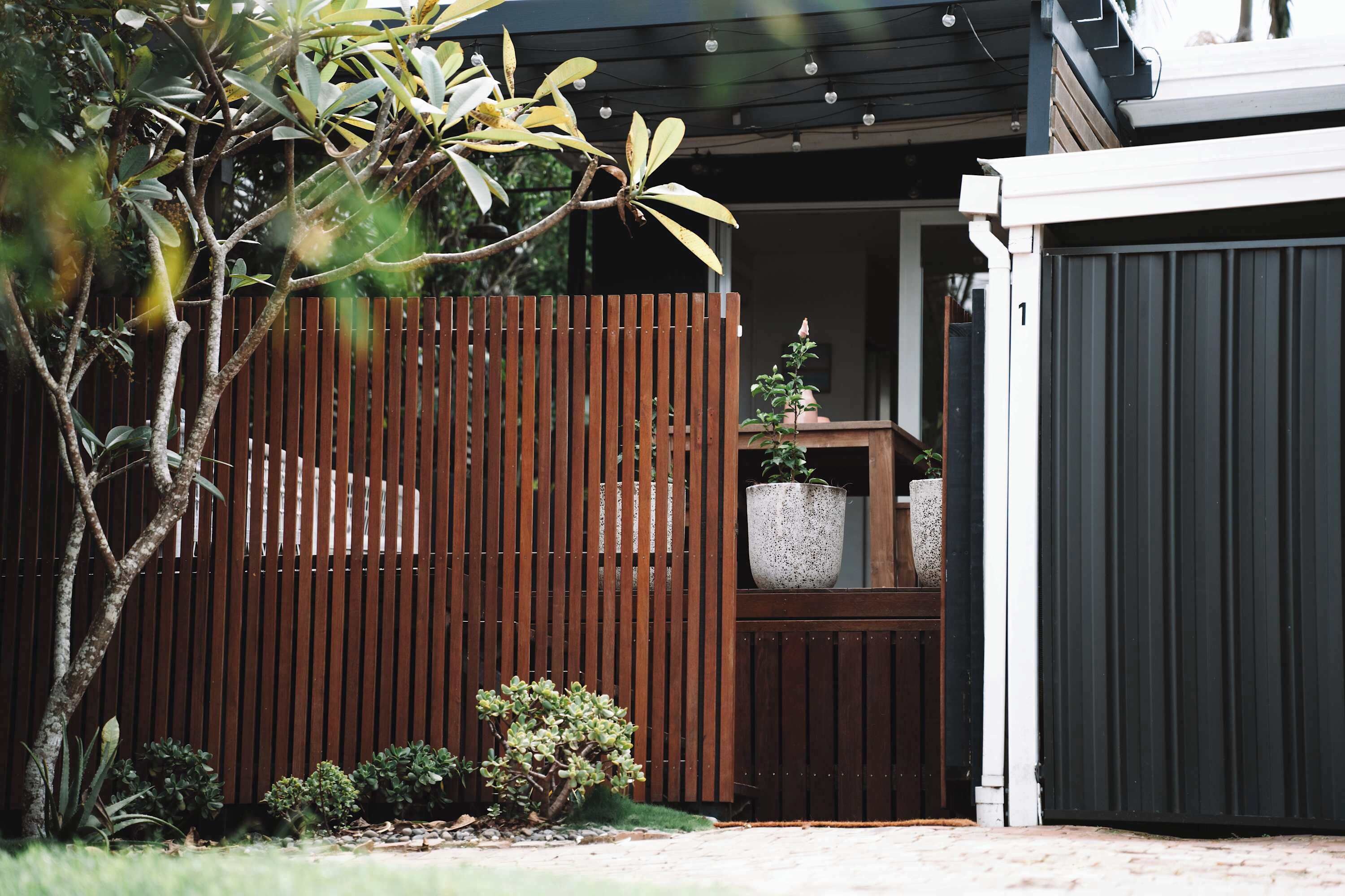 Une clôture en bois, un pot de fleurs et l’entrée d’un bâtiment.