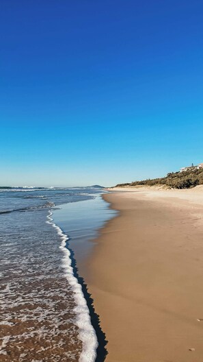 Een strand met helderblauwe luchten en rustige golven.