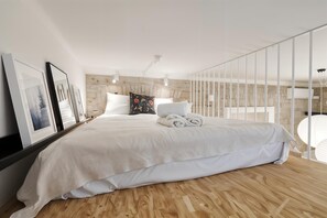 A modern bedroom with a large bed, wooden flooring, and a stone accent wall.