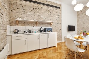 A modern kitchen with white cabinetry, a brick wall, and a dining area with a table set for two.