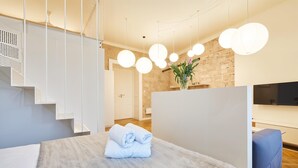 A modern hotel room with a bed, a blue sofa, a flat-screen TV, and a staircase. - Cracow Fancy Brick #2 - Old Town (Kraków)