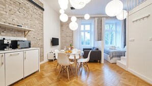 A modern kitchen with a herringbone floor, a dining area with a round table and chairs, and a living area with a sofa and a window. - Cracow Fancy Brick #2 - Old Town (Kraków)