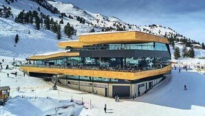 A modern ski resort building with a curved roof and glass facade, surrounded by snow-covered mountains.