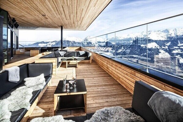A modern, open-plan living area with wooden flooring and furniture, large windows offering a mountain view.