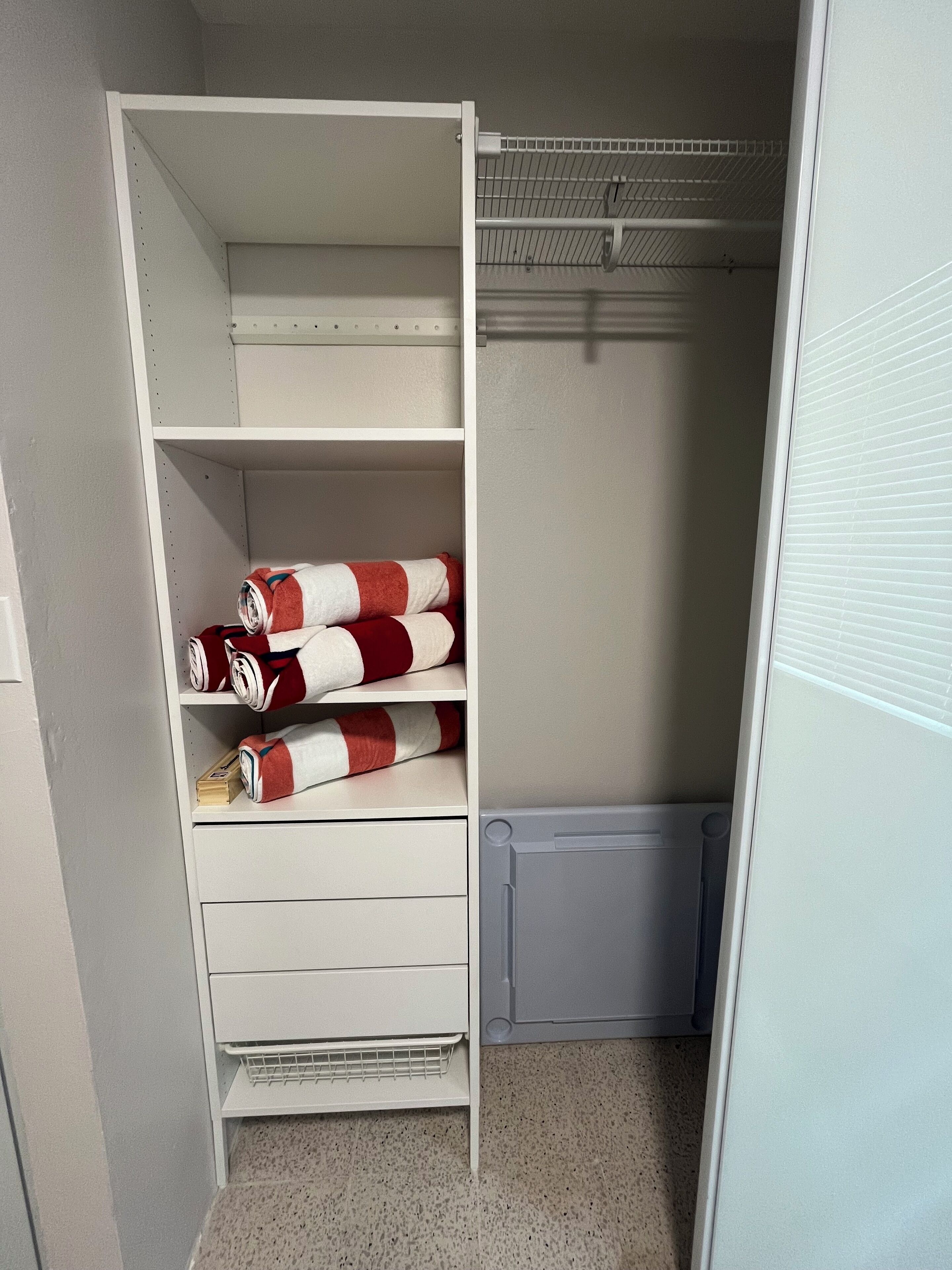 Une armoire blanche dotée de nombreuses étagères et de tiroirs, un radiateur gris et une petite boîte de rangement grise.
