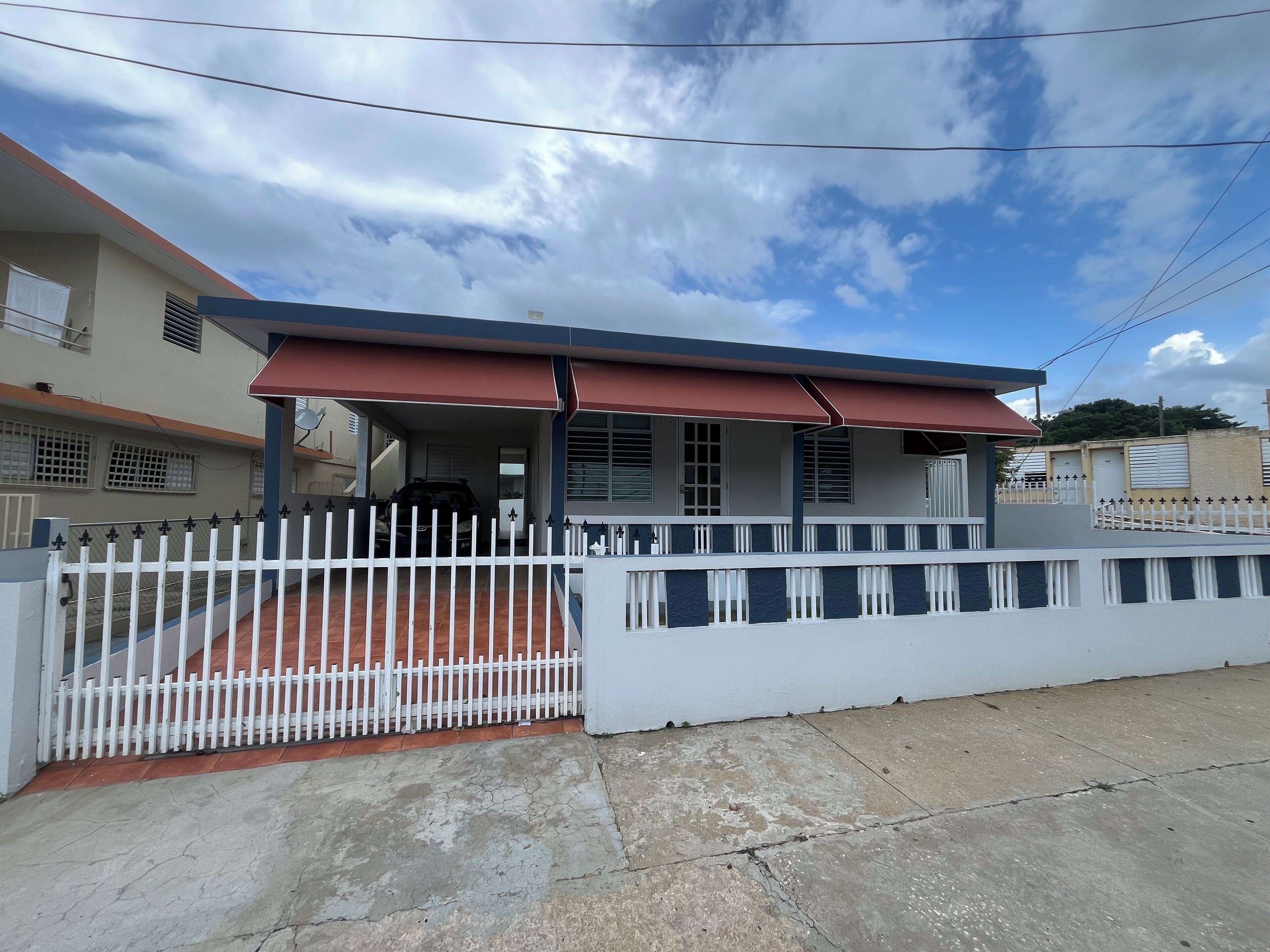 A residential building with a covered porch, white picket fence, and a gated entrance.
