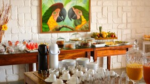 A buffet setup with various food items and a painting of parrots on the wall. - POUSADA AROEIRA (Cairu)