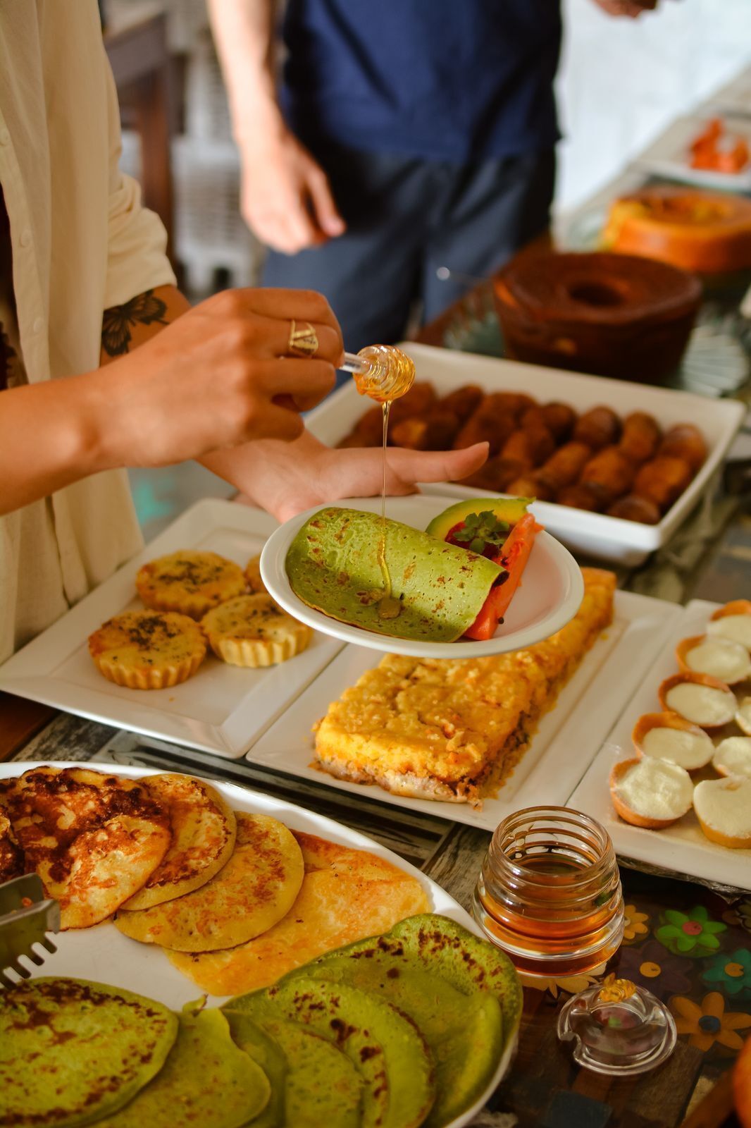 A variety of dishes on a table, including a plate with a rolled vegetable dish, a plate of small pastries, and a glass of honey.