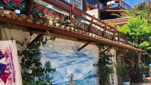 A building with a wooden staircase, a mural of a mermaid, and potted plants. - POUSADA AROEIRA (Cairu)