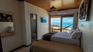 A bedroom with a bed, a window with a view of the beach, and a hammock outside. - POUSADA AROEIRA (Cairu)
