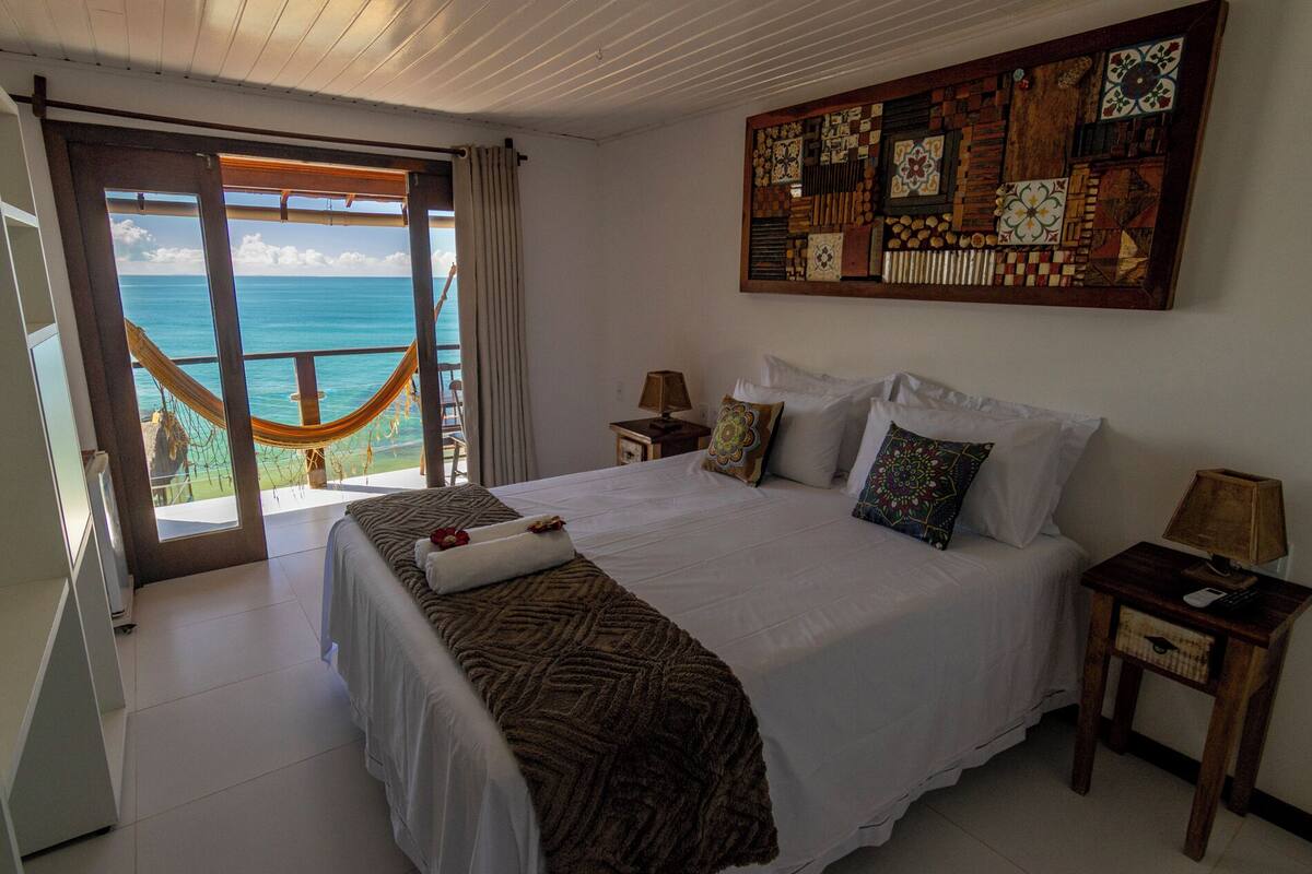 Une chambre avec un grand lit, un hamac et une vue sur l’océan.