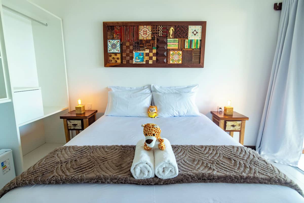 Une chambre d’hôtel avec un grand lit, deux tables de chevet, une œuvre d’art murale et un doudou en forme de girafe posé sur le lit.