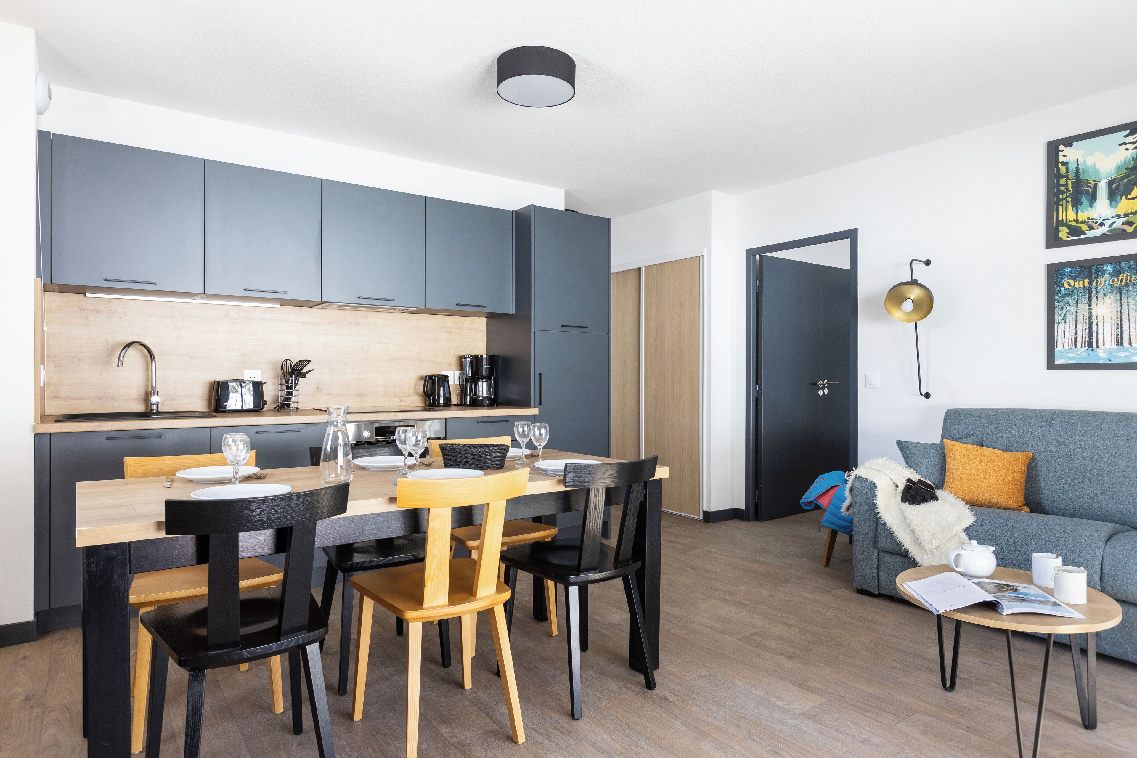 Cocina moderna con armarios grises, una mesa de comedor de madera y sillas negras.