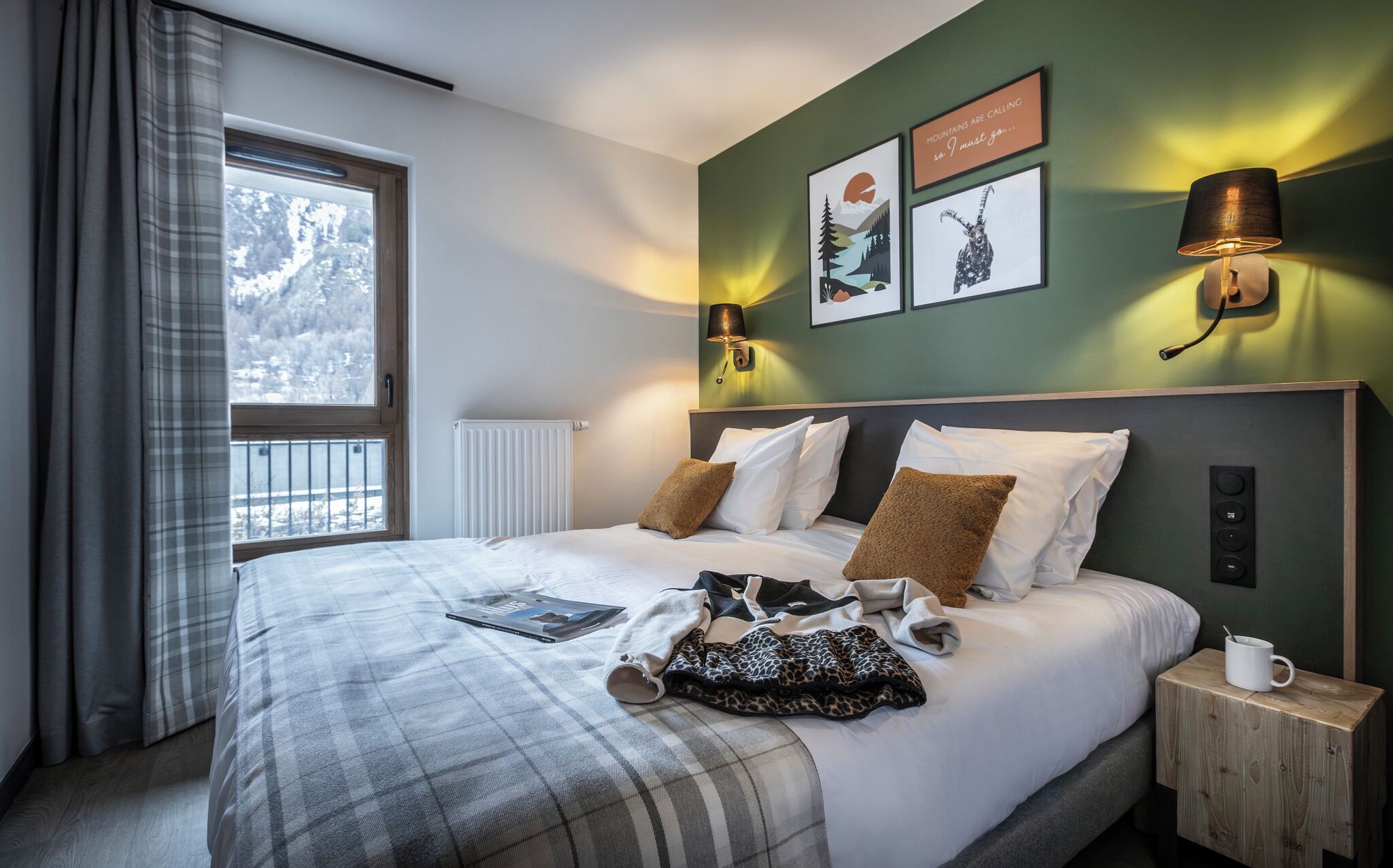 Ein Hotelzimmer mit einem Bett, einem Vorhangfenster, Wandlampen und gerahmten Bildern.