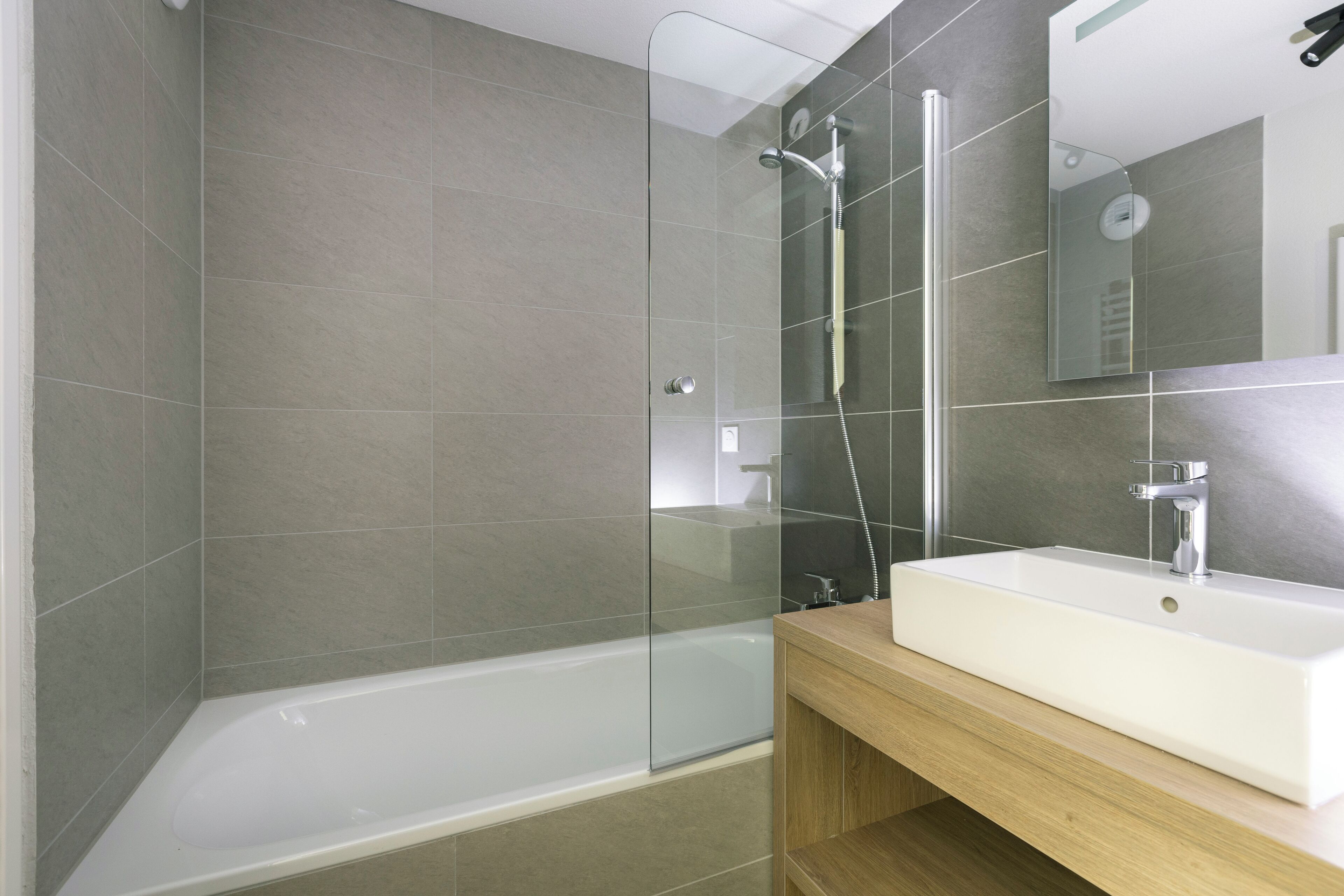 A modern bathroom with a glass-enclosed shower, a white bathtub, and a wooden vanity with a sink.
