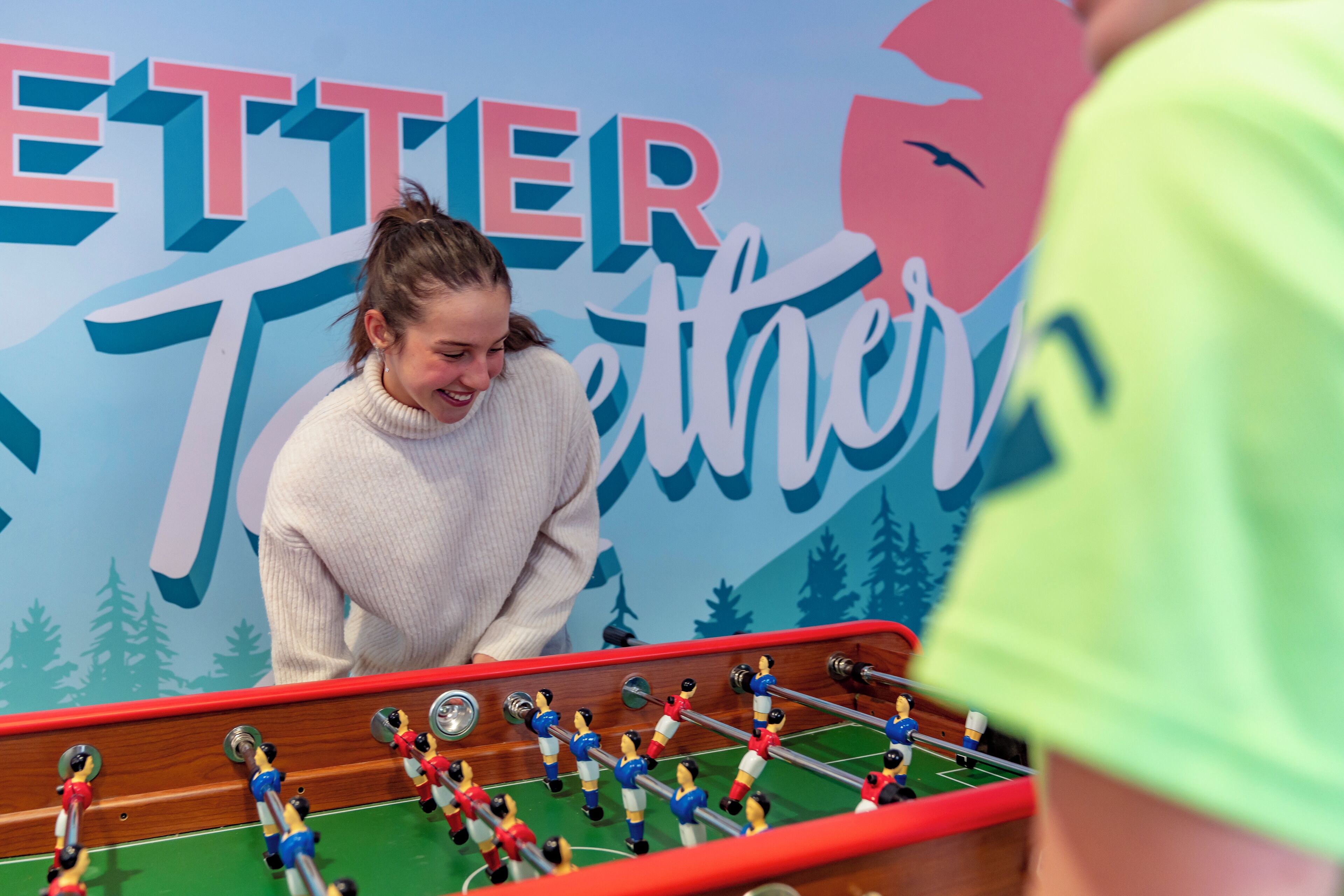 Une personne jouant au baby-foot devant un décor sur lequel on peut lire le texte « ETTER Tetter ».