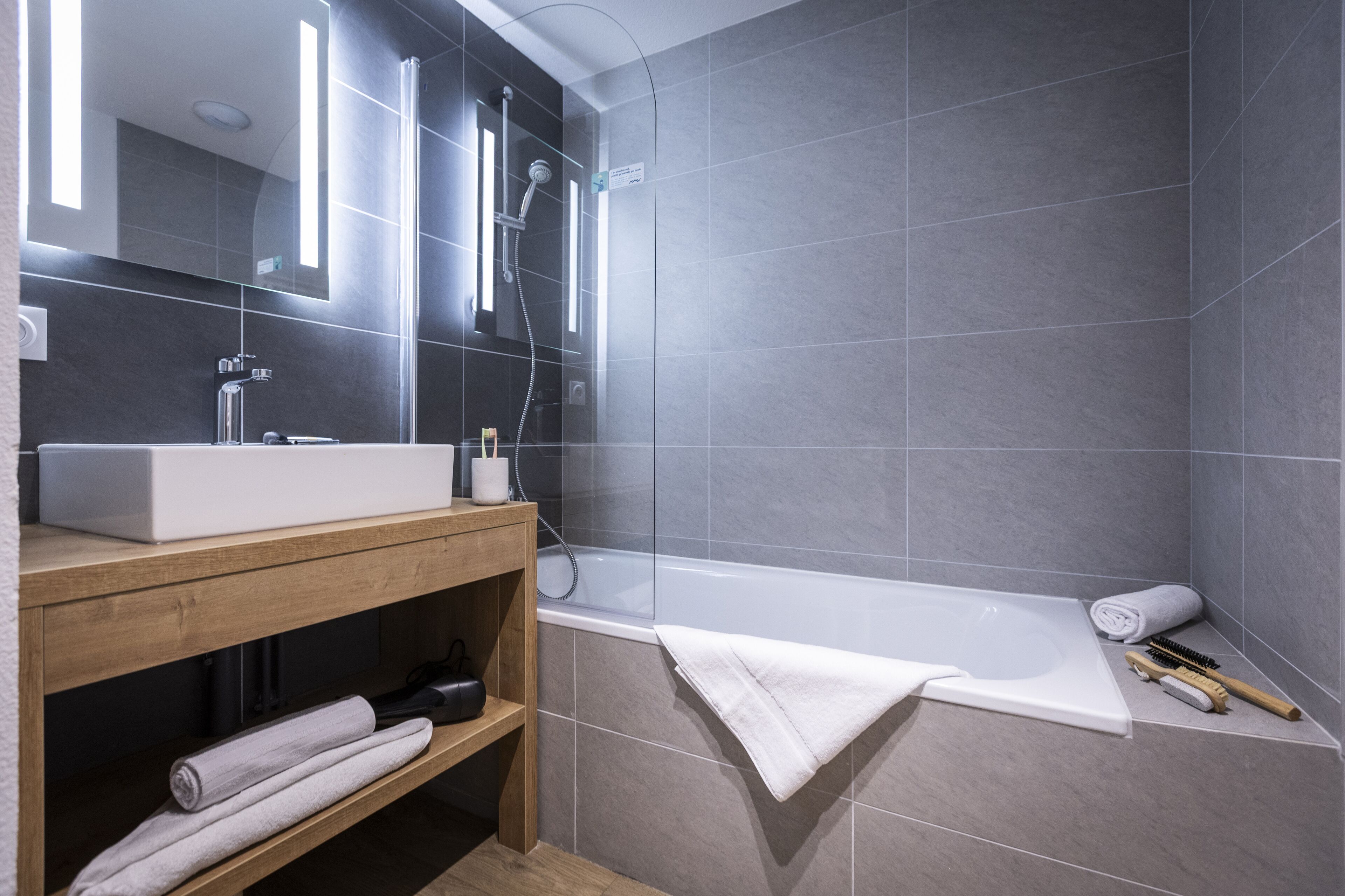 Une salle de bain moderne avec une grande baignoire, un meuble-lavabo en bois et un miroir.