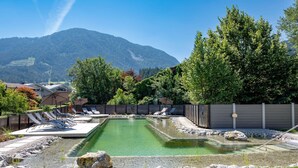 Zona de piscina con sillas de descanso, un pequeño estanque y montañas al fondo.