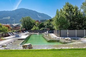 A pool area with lounge chairs, a small pond, and a mountain backdrop. - Penthouse in Brixental (Brixen im Thale)