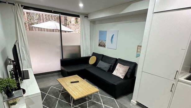 A modern living room with a sectional sofa, a coffee table, a TV, and a kitchen area.