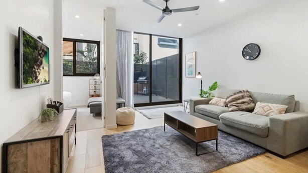 Un salon moderne avec un canapé gris, une table basse et un téléviseur posé sur un meuble en bois.