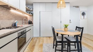 Une cuisine moderne équipée d’une cuisinière à gaz, de meubles blancs et d’un coin repas avec une table et des chaises en bois.