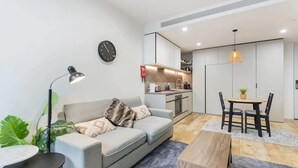 Un salon moderne comprenant un canapé, une table basse, une table à manger avec des chaises, un coin cuisine et une horloge murale.