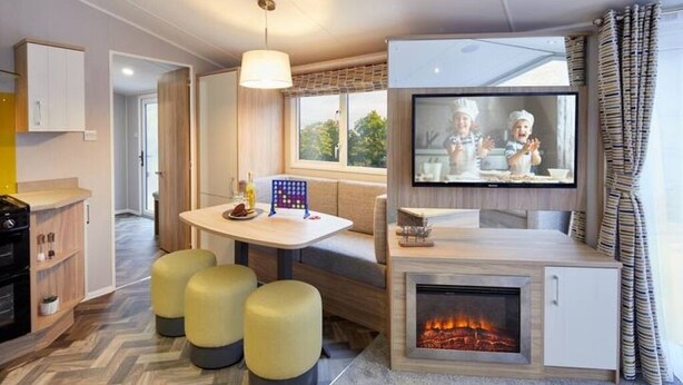 Una cocina moderna con estufa integrada, una zona de comedor con mesa y sillas, y un televisor montado sobre la estufa.