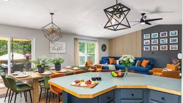 A modern kitchen with a central island, dining area, and a living space with a blue sofa and decorative pillows.