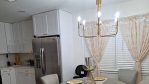 Una cocina moderna con armarios blancos, un refrigerador de acero inoxidable y un comedor con una mesa redonda dispuesta para cuatro comensales.