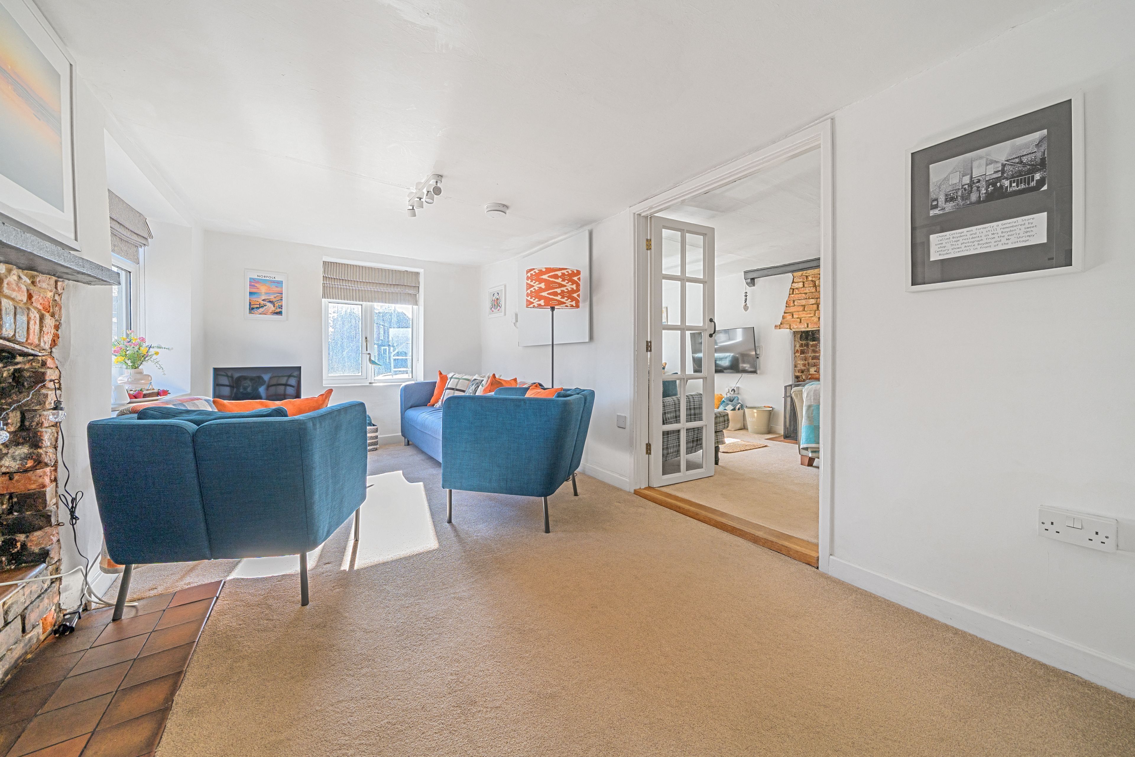 Un salon spacieux avec une cheminée, deux fauteuils bleus, une table basse et une grande fenêtre.