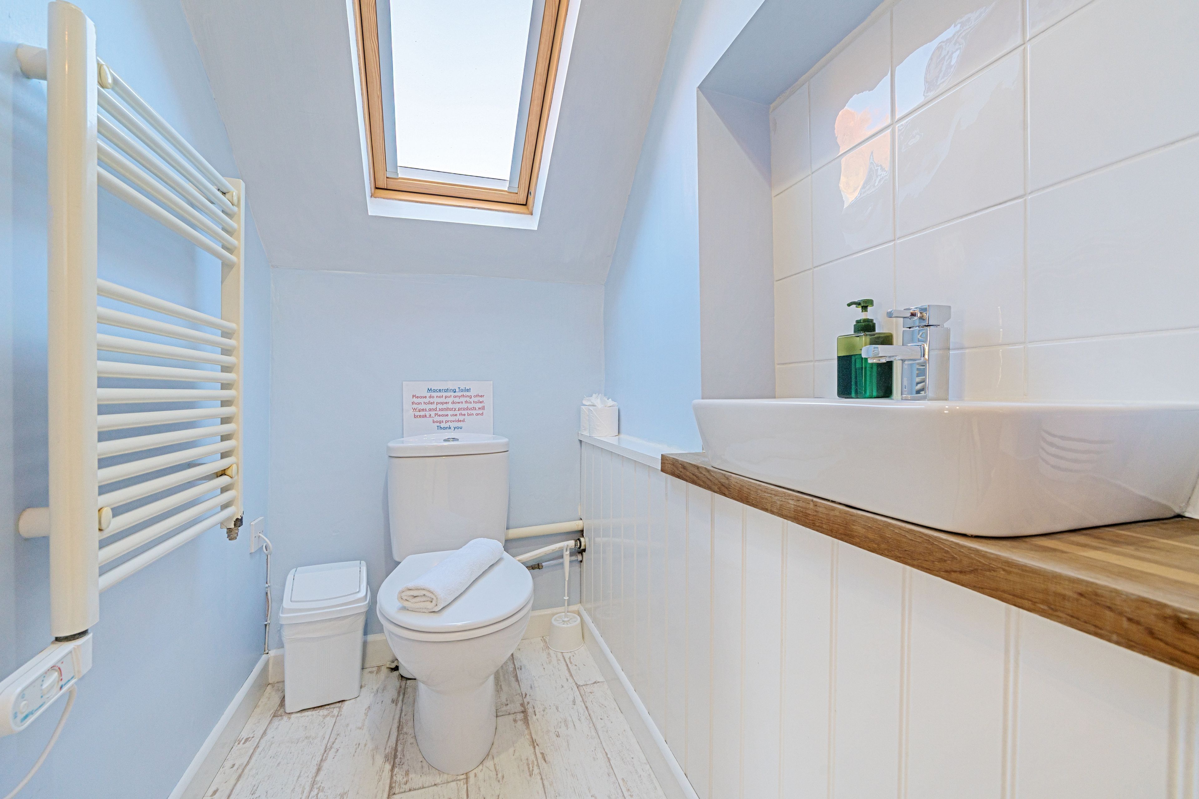 A bathroom with a skylight, a toilet, a sink with toiletries, and a wooden shelf.