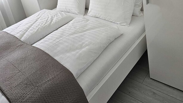 A modern bedroom with a bed, white bedding, a decorative wall piece, and a wardrobe.