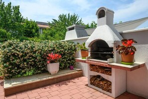 An outdoor brick patio with a stone-built barbecue grill and a white chimney. - Apartment SoMi 1 (Porec)