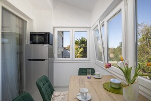 A compact kitchen with a refrigerator, a microwave, and a window overlooking a garden.