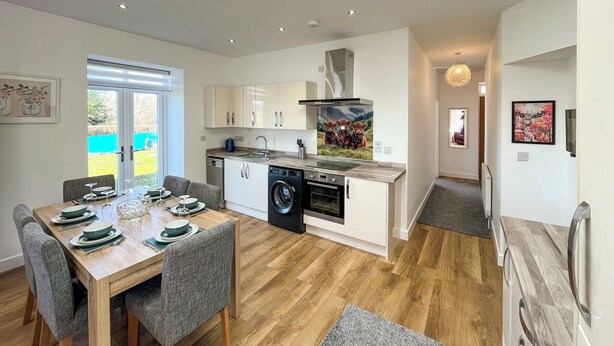 A modern kitchen with built-in appliances, a dining area with a table set for four, and a view of the outdoors.