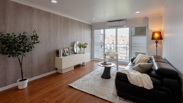 Un salon moderne avec un plancher en bois, un canapé en cuir noir, une console blanche, une plante en pot et une grande fenêtre donnant sur des immeubles.