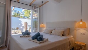 A bedroom with a large bed, two bedside lamps, a view of the outdoors, and a small wooden side table.
