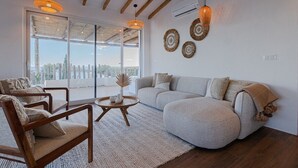 A modern living room with a grey sofa, wooden chairs, a round coffee table, and a large window offering a city view.