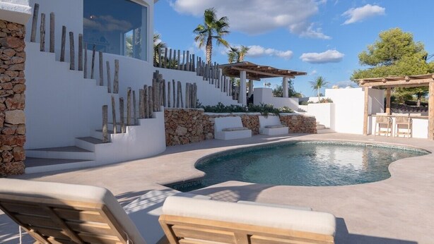 A modern pool area with a curved pool, white walls, stone accents, and outdoor seating.