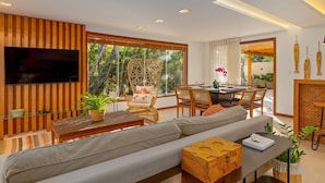 A modern living room with a sofa, wooden accents, a TV, and a dining area with chairs and a table. - Bz15 Casa 200 metros da praia 4 suítes (Buzios)