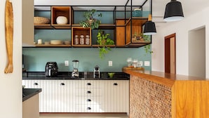 A modern kitchen with white cabinetry, black countertops, and wooden accents. There are multiple shelves with plants and kitchenware, and a black pendant light hangs above the counter. - Bz15 Casa 200 metros da praia 4 suítes (Buzios)