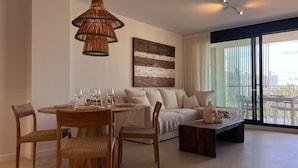 Ein modernes Wohnzimmer mit einer Couch, einem Esstisch mit Stühlen, einem Couchtisch und einem großen Fenster mit Stadtblick.