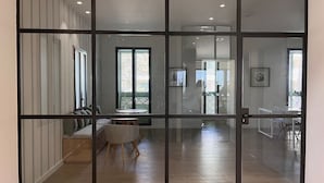 Een modern interieur met een glazen scheiding, een zithoek met kussens en een eethoek met een tafel en stoelen.