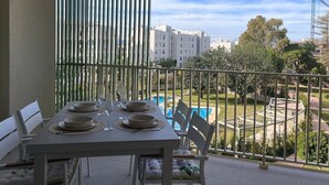 Ein Balkon mit Tisch für vier Personen, mit Blick auf einen Pool und Grünflächen.