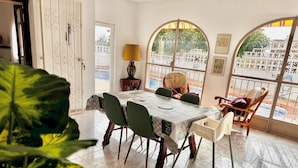Un coin repas avec une table dressée pour quatre personnes, entourée de chaises, d’une lampe et offrant une vue par une fenêtre agrémentée d’un paravent décoratif.