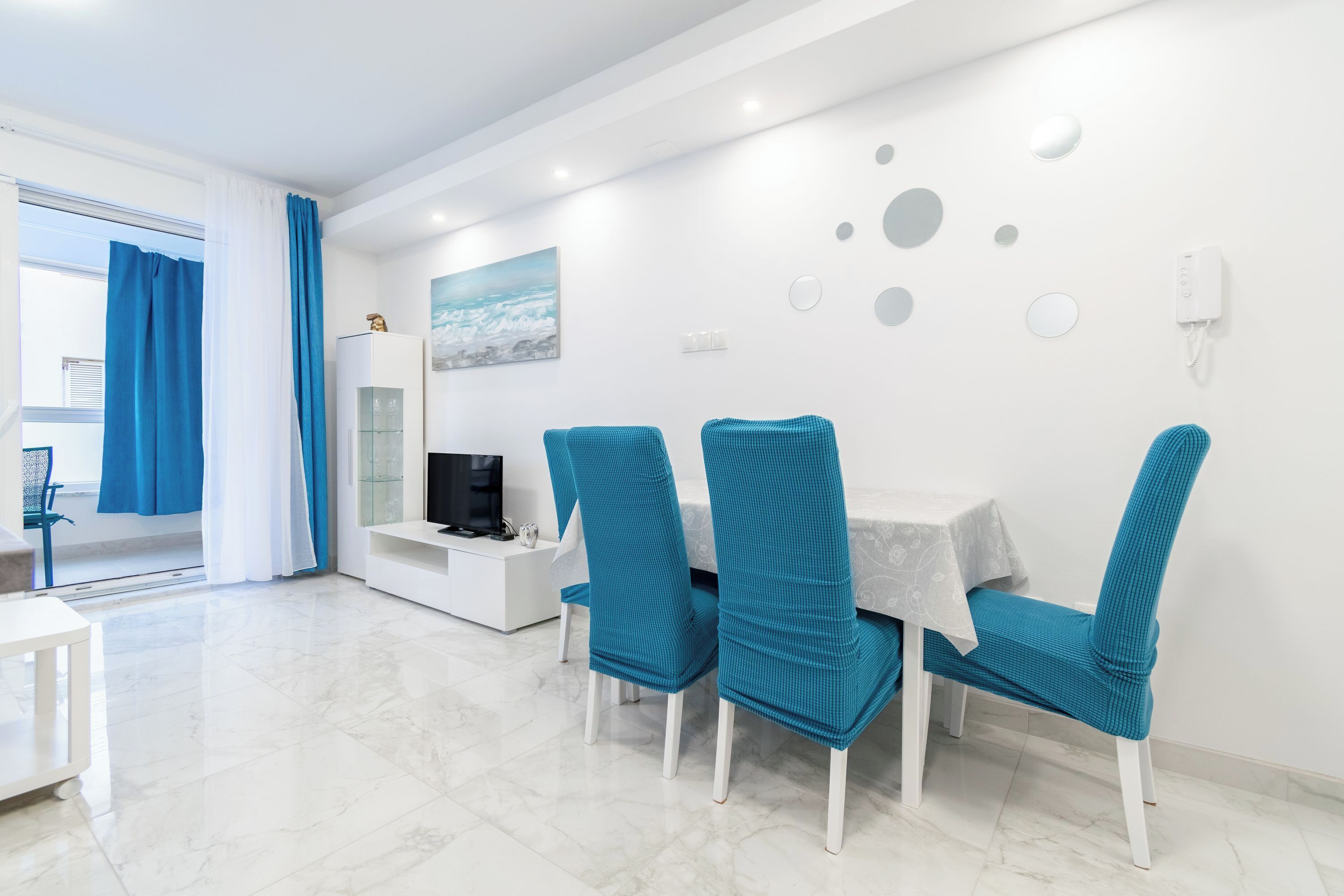 A modern dining area with a white table and four teal chairs.