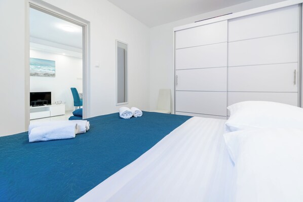 A hotel room with a bed, a blue carpet, a large mirror, a TV, and a wardrobe. - Modern apartment Marijan (Makarska)
