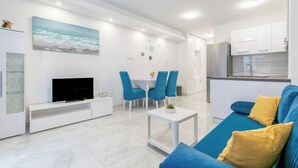 A modern living room with a flat-screen TV, a blue sofa, and a dining area with blue chairs. - Modern apartment Marijan  (Makarska)